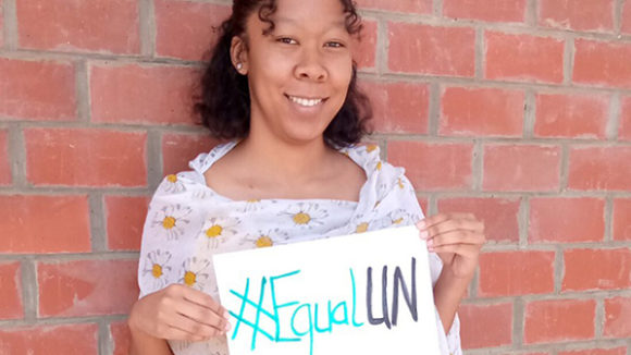 A woman stands holding a hand written equal UN sign