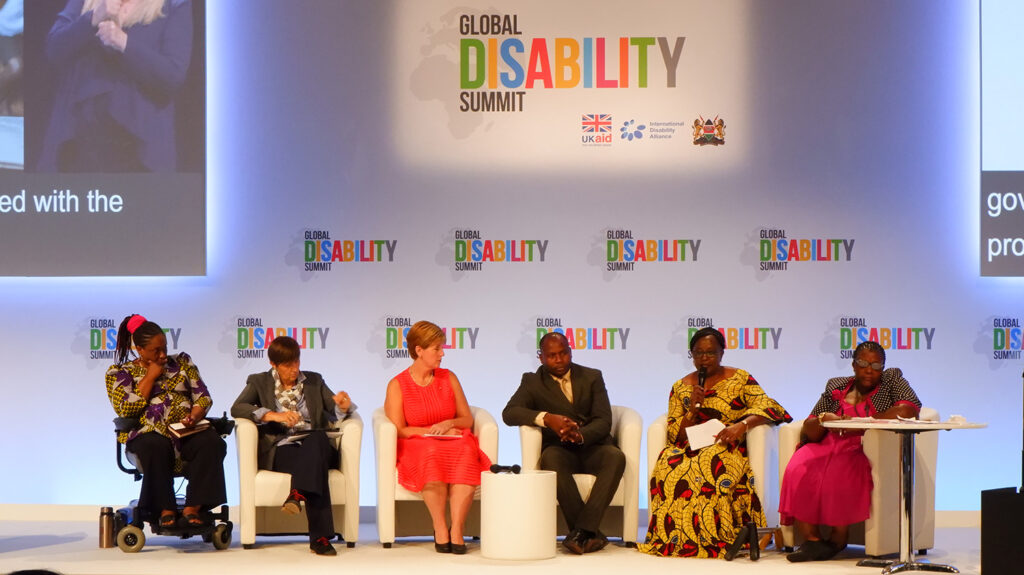 Six speakers sit on stage during a panel discussion at the Global Disability Summit 2018.