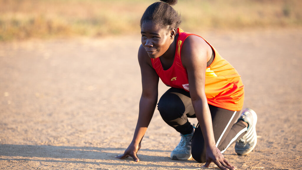Athlete Taonere Banda crouches on the ground, ready to start a training run.