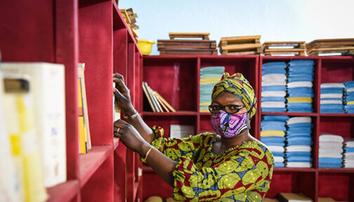 A woman wearing a face mask, standing by shelves in a school building.