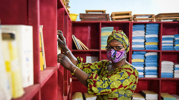 A woman wearing a face mask, standing by shelves in a school building.