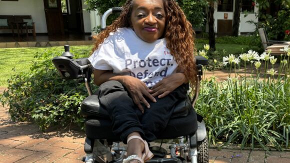 Photo of Florence in a white t-shirt and her wheelchair, smiling to the camera