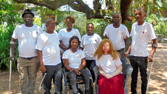 A group of people wearing T-shirts featuring the Equal Zimbabwe logo. Some of them have visible physical disabilities.