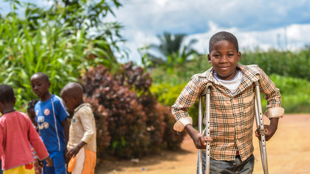 A young boy with crutches smiles at the camera.